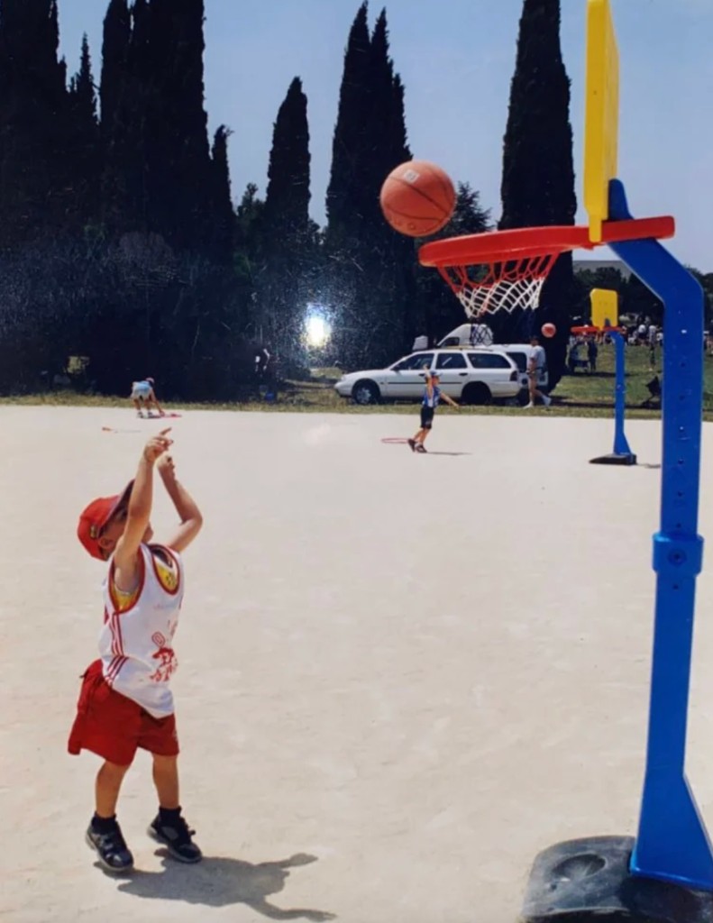 Quentin enfant, en train de tirer au panier sur un terrain de basket extérieur.